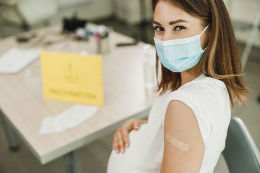 A pregnant woman sitting and holding her belly after receiving a coronavirus vaccine. Looking at camera.