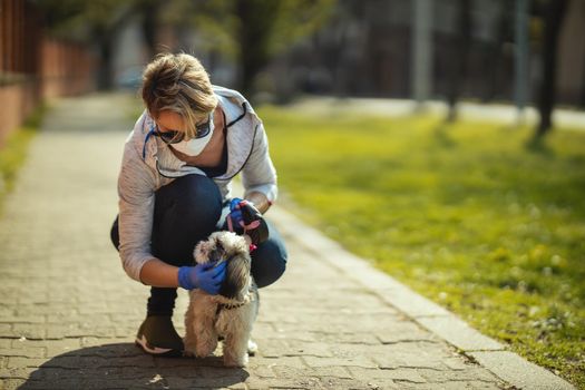 A woman in a medical protective mask is walking along the city street path with her dear cute little Shih Tzu dog during flu virus outbreak and coronavirus epidemic.