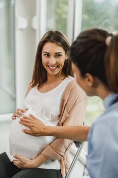 Attractive pregnant woman talking to nurse while waits for gynecologist check up.