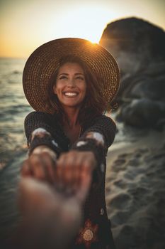 A beautiful young woman is having fun and relaxing on the beach at the sunset. She extends hands to someone whose hand is seen.