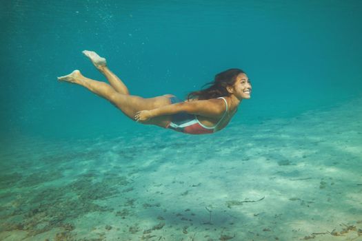 A beautiful young woman is having fun at summer vacation exploring seafloor during scuba diving in sea.