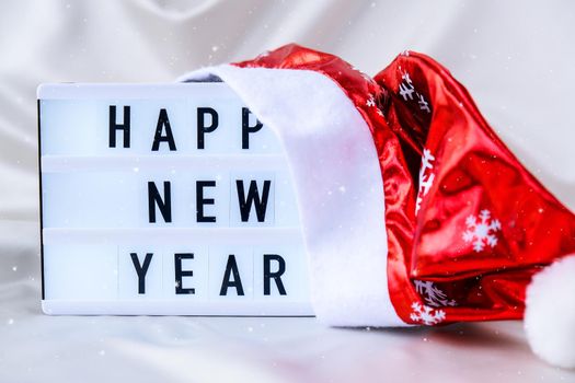 Lightbox with text HAPPY NEW YEAR with santa hat on silk fabric background. Winter holiday concept. Christmas and New Year