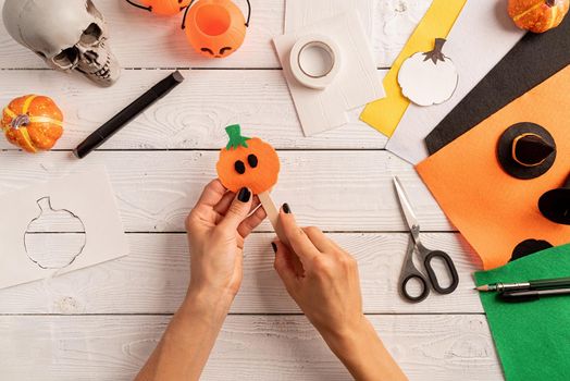 Happy Halloween concept. Step by step instruction of making halloween bookmark DIY pumpkin craft. Step 6 - stick a pumpkin and the ice cream stick. Bookmark is ready. Top view flat lay