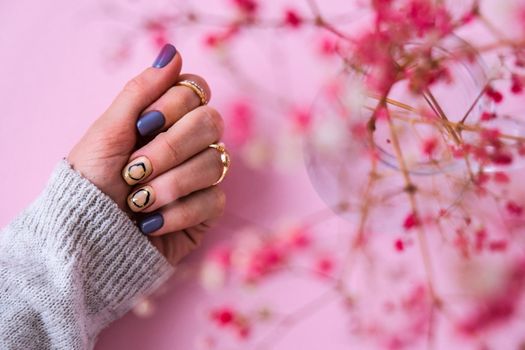 Hand in sweater and pink flowers with modern manicure nails. Female hand. Glamorous beautiful manicure. Manicure salon concept. Nail polish close up.