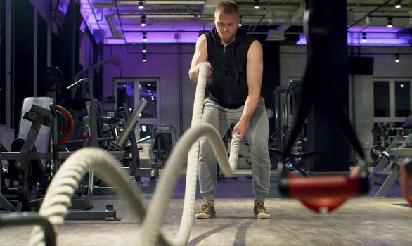 Man bodybuilder doing exercise using battle ropes in gym. Fitness, sport, exercising, training and lifestyle concept.