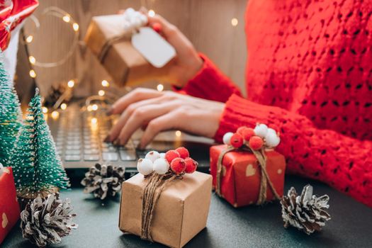 Christmas online shopping, work and education. New Year decorations on table. Woman with notebook computer at home. Winter holidays sales. Gift boxes, christmas trees. Garland light