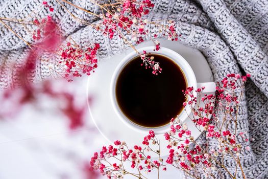 Cup of black coffee on white background with sweater and bright pink flowers. Flat lay. Copy space. Fashion concept. Cozy lifestyle. Still life