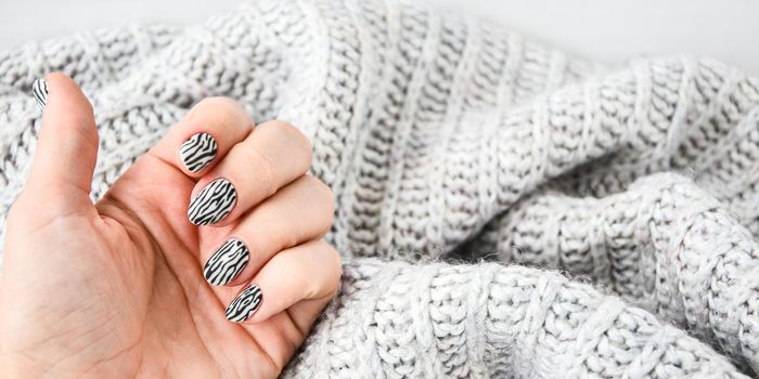 Hand in sweater with zebra animal printed nails. Female manicure. Glamorous beautiful manicure. Manicure salon concept. Nail polish close up.