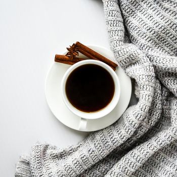 Cup of coffee with cinnamon sticks and anise star on white background. Sweater around. Winter morning routine. Coffee break. Copy space. Top view. Breakfast. Flat lay