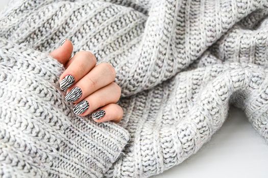 Hand in sweater with zebra animal printed nails. Female manicure. Glamorous beautiful manicure. Manicure salon concept. Nail polish close up.