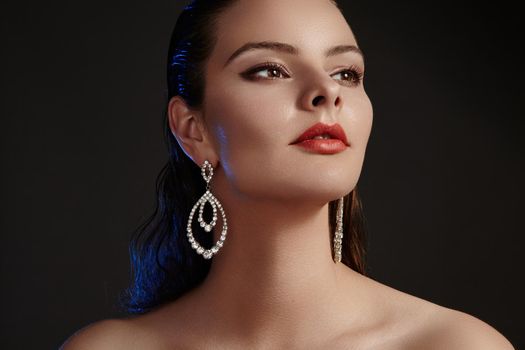 Beautiful woman in luxury fashion earrings. Diamond shiny jewelry with brilliants. Sexy retro style portrait. Model with glamour accessories jewelery, fashion makeup, clean shiny skin and wet hair