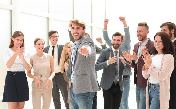 happy business man standing among colleagues and pointing at you. success concept