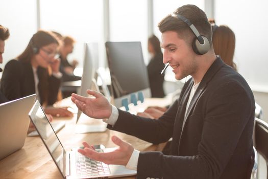 side view. a business man in a headset is working on a laptop.