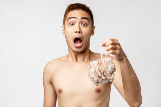 Beauty, people and hygiene concept. Shocked and amused young handsome asian man gasping as someone come in bathroom while he washing, standing naked holding bath sponge.