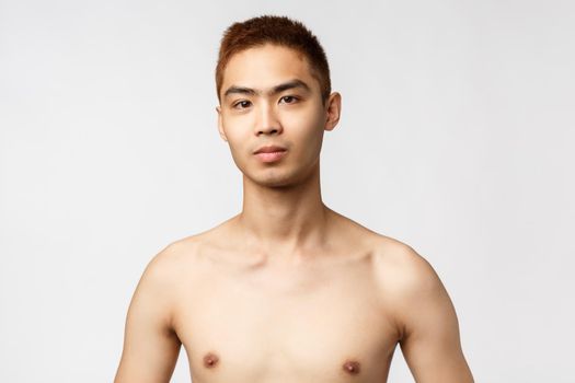 Beauty, people and home concept. Close-up portrait of handsome young asian man with naked torso, looking camera confident and pleased, standing white background, go to shower.