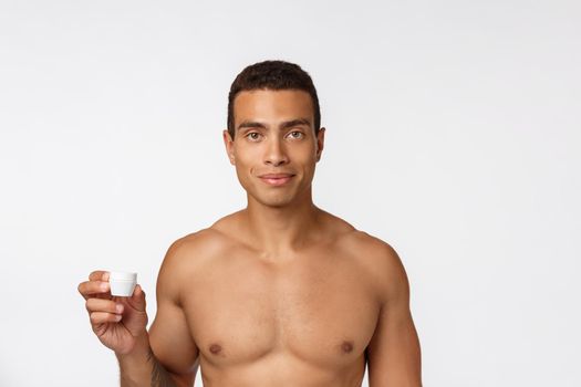 Photo of shirtless african american man smiling and applying face cream isolated over white background.