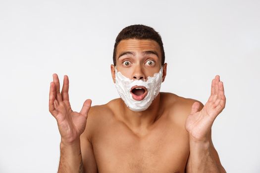 Close up of a happy naked african man with face in shaving foam isolated over gray background.