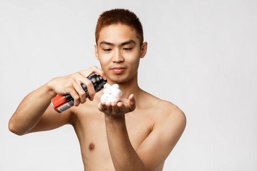 Beauty, people and hygiene concept. Portrait of asian handsome man with naked torso want to shave bristle, smiling pleased as use shaving cream, standing white background.