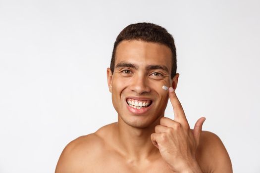 Photo of shirtless african american man smiling and applying face cream isolated over white background.