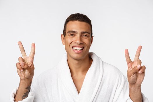 Closeup portrait happy, excited, successful young man giving peace, victory or two sign, isolated white background