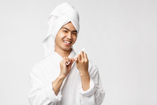 Beauty, spa and leisure concept. Handsome silly asian man taking care of hygiene, polish nails, making manicure while staying at home relaxing during covid19 outbreak qurantine, smile pleased.