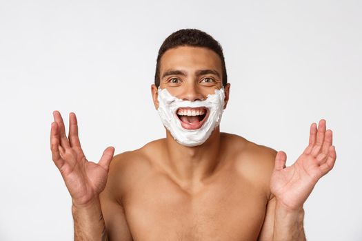 Close up of a happy naked african man with face in shaving foam isolated over gray background.