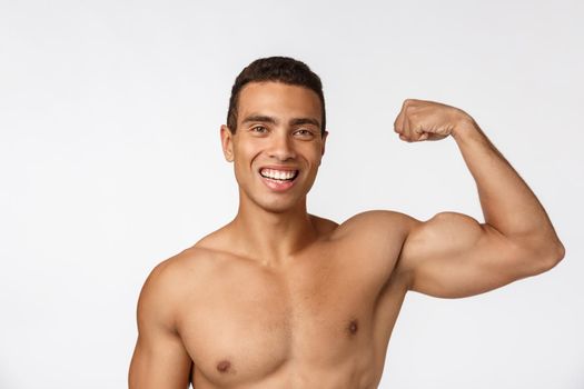 African American teenager shows muscles on arm. Isolated on white background. Studio portrait. Transitional age concept