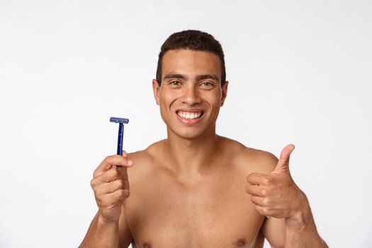 Close up of a happy naked african man holding razor isolated over gray background