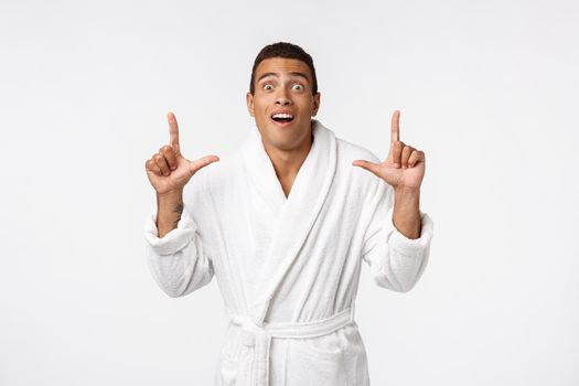 African american guy wearing a bathrobe pointing finger with surprise and happy emotion. Isolated over whtie background