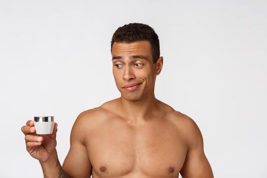 Photo of shirtless african american man smiling and applying face cream isolated over white background.