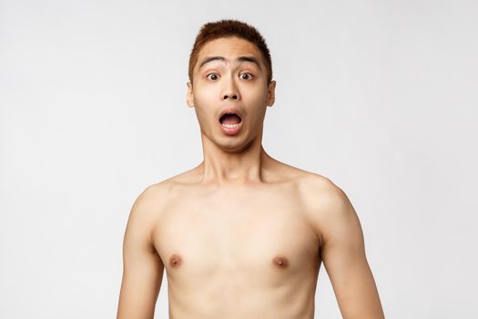 Beauty, people and home concept. Portrait of shocked gasping asian man with naked torso look excited and shook camera, open mouth amazed and astonished, standing white background. Copy space