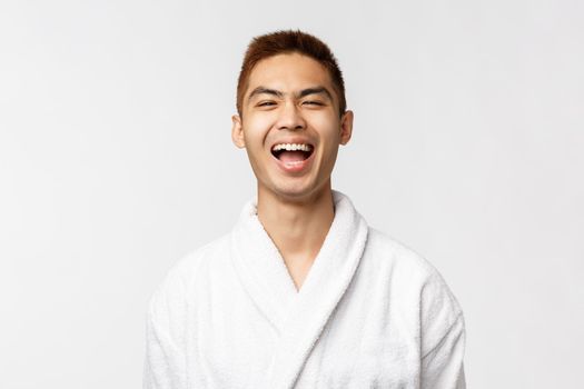 Beauty, spa and leisure concept. Cheerful asian man spending weekends to relax at hot springs, wear bathrobe laughing, enjoying vacation, having rest at hotel resort, standing white background.