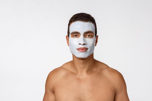 Picture of cheerful nice young african guy smiling on camera. Portrait of man with cream mask on cheeks. Beauty routine.