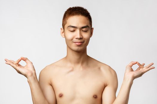 Beauty, people and home concept. Close-up portrait of happy, relieved asian man standing naked over white background, close eyes and smiling, meditating to stay relaxed and calm.