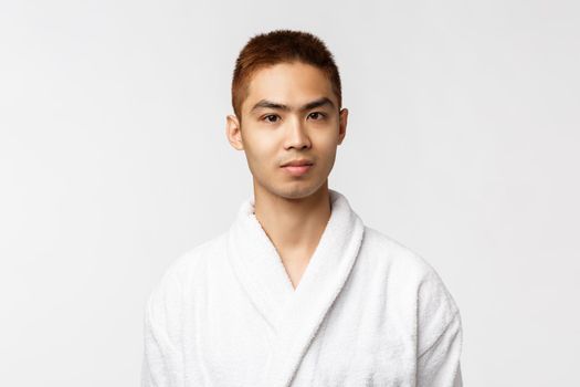 Beauty, spa and leisure concept. Young asian man enjoying vacation, spend weekends on hot springs, wearing bathrobe and smiling camera, feel relaxed at beauty salon, white background.