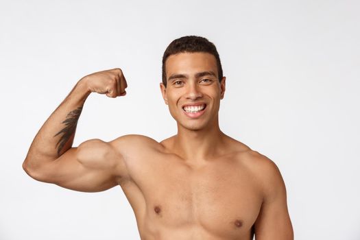 African American teenager shows muscles on arm. Isolated on white background. Studio portrait. Transitional age concept