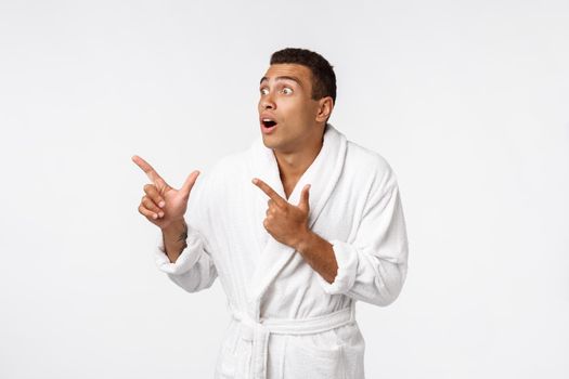 African american guy wearing a bathrobe pointing finger with surprise and happy emotion. Isolated over whtie background