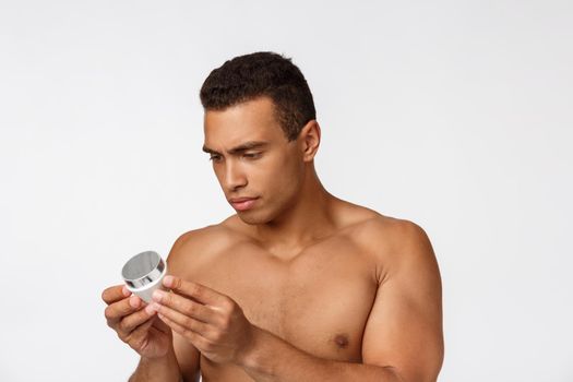 Photo of shirtless african american man smiling and holding cream isolated over white background.