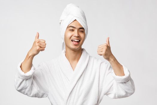 Beauty, spa and leisure concept. Cheerful, happy smiling asian man in bathrobe show thumbs-up, recommend and approve great resort, awesome hotel, look upbeat, white background. Copy space