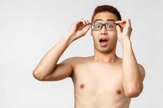 Beauty, people and lifestyle concept. Close-up portrait of asian naked man put-on glasses and gasping impressed, open mouth shocked, standing amused white background. Copy space