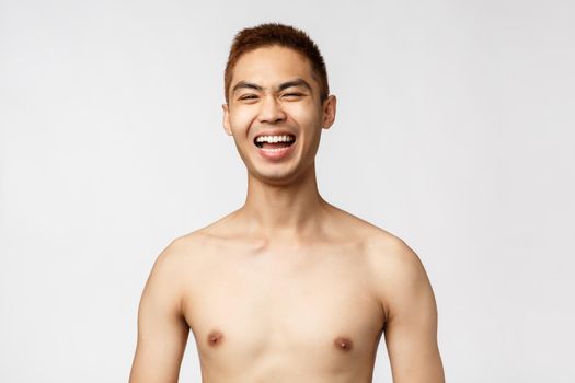 Beauty, people and home concept. Close-up portrait of handsome cheerful asian man, laughing out loud, standing naked torso and smiling pleased, standing white background enthusiastic.