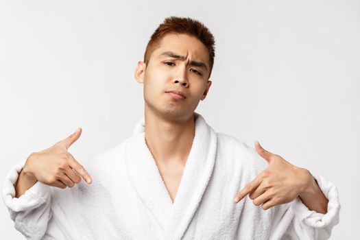 Beauty, spa and leisure concept. I am boss here. Portrait of sassy and cool asian rich man relaxing in resort, pointing himself and frowning, show-off his ego, standing white background.