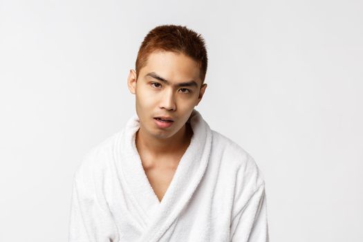 Beauty, spa and leisure concept. So lame. Portrait of reluctant and indifferent asian man in bathrobe, open mouth and say blah, feel bored and indifferent, hear boring conversation, white background.