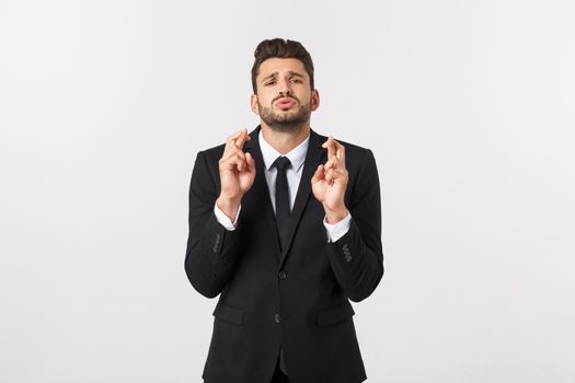 Businessman fingers cross on copy space. Handsome young man in suit looking at camera while standing against white background