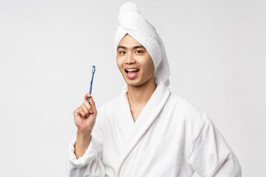 Beauty, spa and leisure concept. Cheerful handsome asian man in bathrobe and bath towel, showing toothbrush and smiling upbeat, washing-up at morning, prepare for big day, white background.