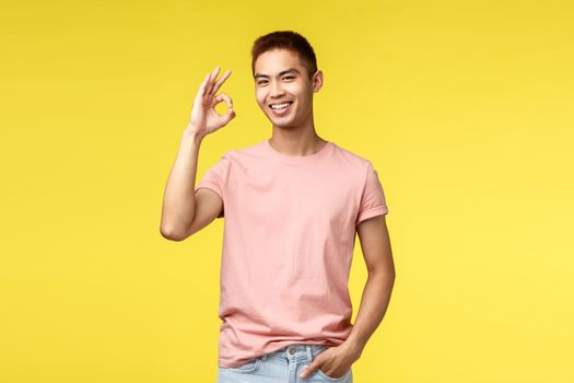 Lifestyle, travel and people concept. Nice quality, guarantee. Portrait of cheerful asian man showing okay, good sign and smiling joyfully, rate excellent product, approve and agree plan.