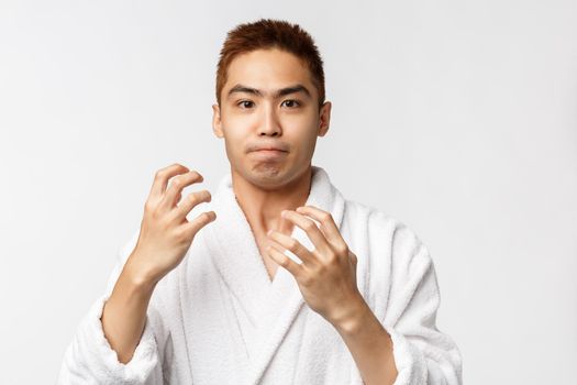 Beauty, spa and leisure concept. Portrait of bothered, fed up asian man in bathrobe, raising hands in dismay react to failure, losing competition, being disappointed with results, white background.