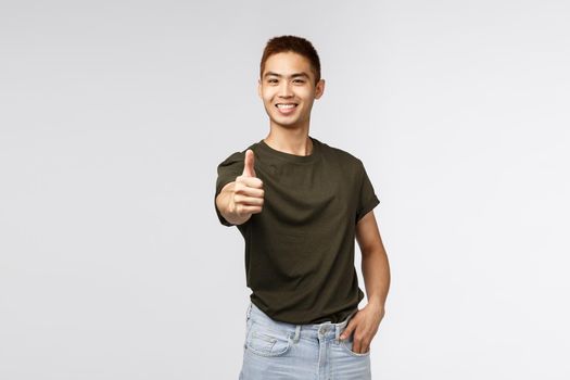 Very good, excellent job. Portrait of happy, pleased asian man thumb-up with extended hand and smiling, encourage keep up nice work, being satisfied and recommend product, grey background.