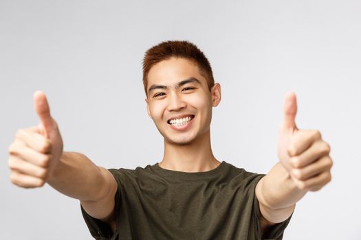 People, different expressions and lifestyle concept. Close-up portrait of enthusiastic japanese guy saying yes, approve product, give recommendation and guarantee best quality, thumbs-up.