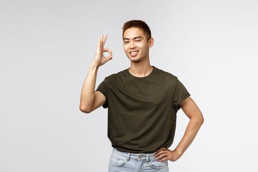 No problem, leave it to me. Satisfied and confident, assertive young asian man standing relaxed and carefree, wink encourage friend, show okay sign guarantee best quality, recommend service.
